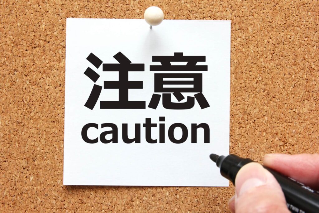 コルクボードに貼ってある「注意caution」と書かれた白い紙と、ペンを持っている右手