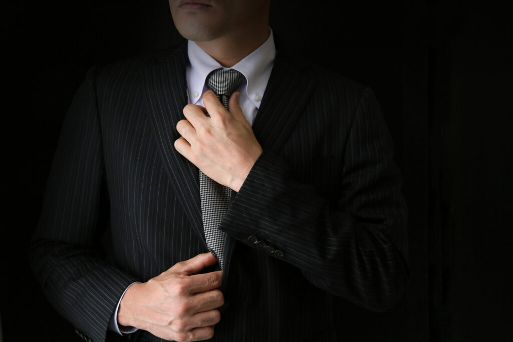 左手でネクタイを締め直しているスーツ姿の男性