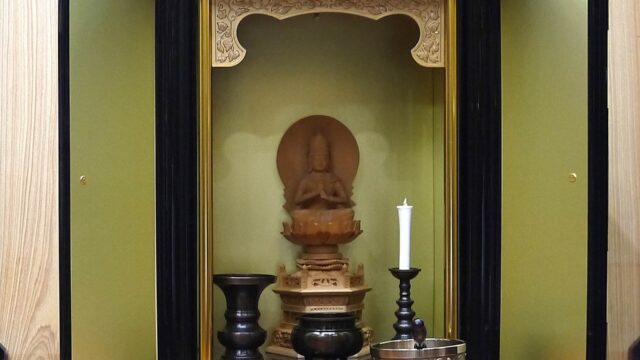 仏壇の中にある木造の大日如来像とろうそくと香炉と花瓶とお鈴