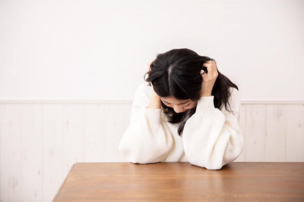 両肘をテーブルにつきながら両手で両耳を覆ってうつむいている白いセーターを着た女性