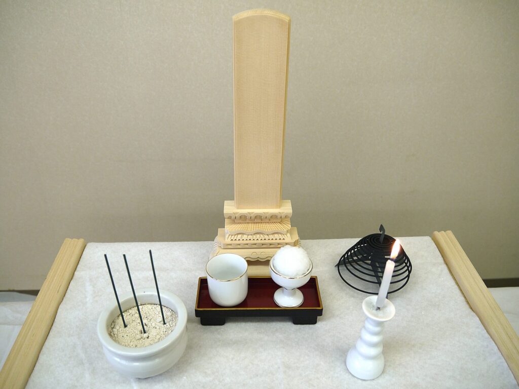 白木の経机の上にある香炉、ろうそく、仏飯、茶器、渦巻き香、白木位牌